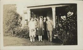 Three men,two ladies and child in front of veranda