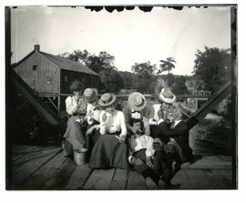 [Five women and two men eating candy canes, sitting on a bridge, possibly Gananoque?]