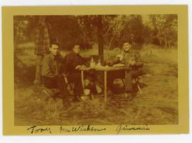 Colour snapshot of 3 men at a table in a clearing, faded to yellow, inscribed “Tony Mr Wishbow Ji...